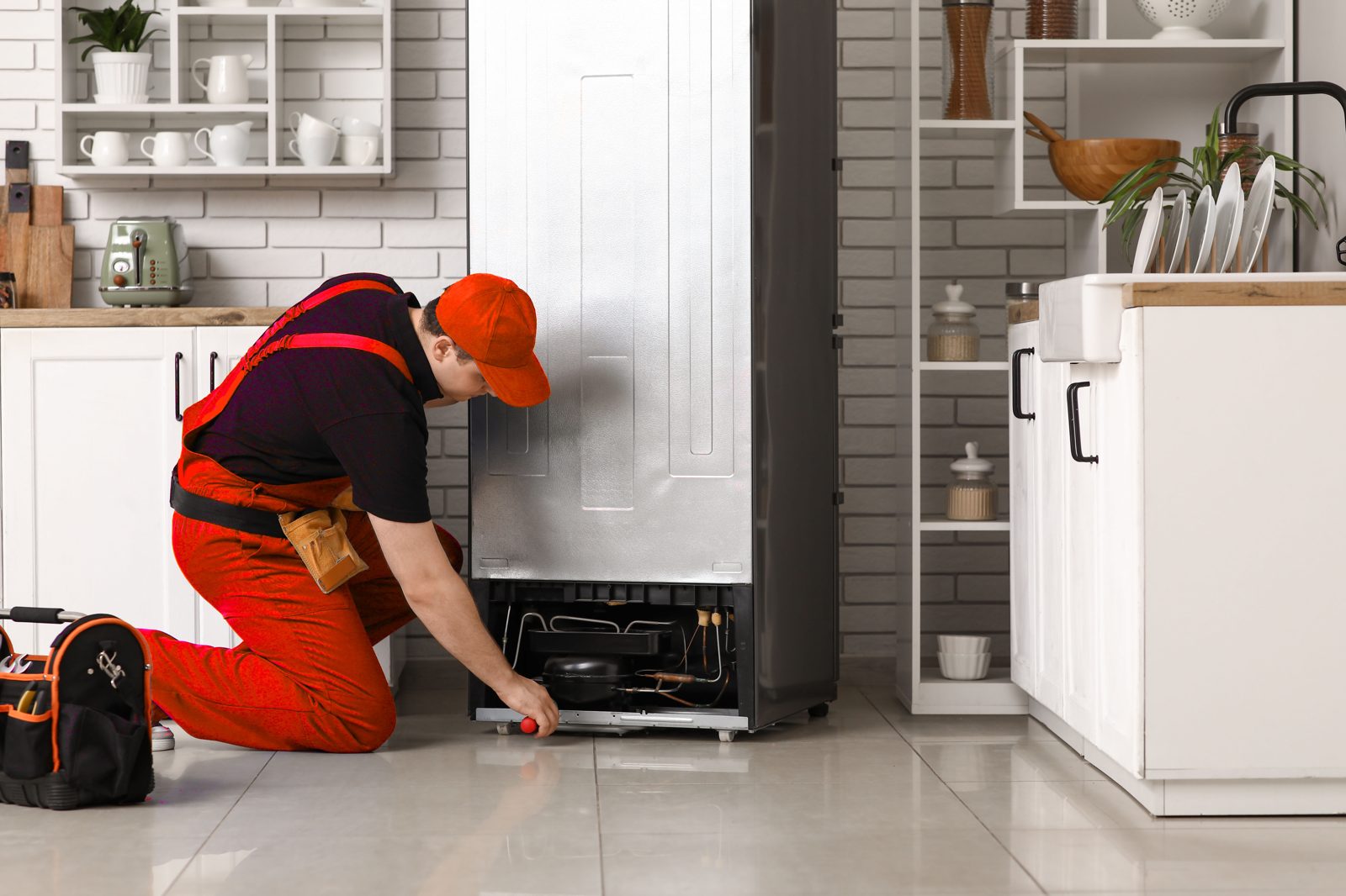 Technician repairing a black refrigerator in a bright kitchen